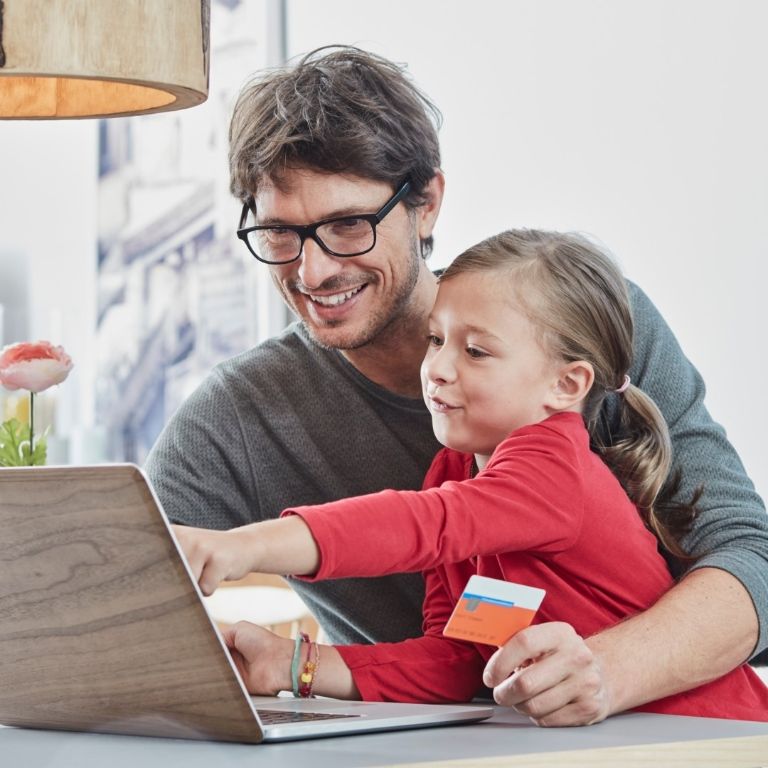 Happy father and daughter with a card using laptop on table at home.